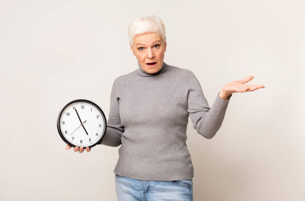 istock Shocked elderly woman holding wall clock and gesturing with hand 1171060765