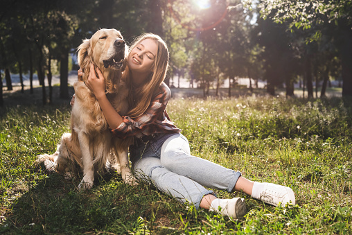 full length view of beautiful girl smiling while petting golden retriever and looking at dog