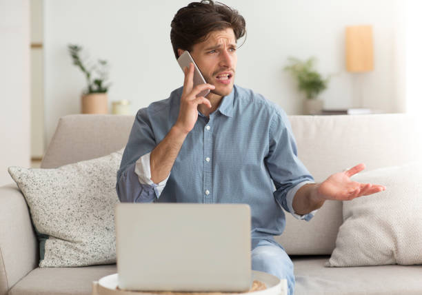 istock Unsatisfied Guy Complaining About Problems With Laptop By Phone Indoor 1171061444