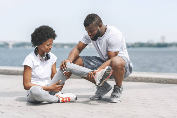 Afro Guy Helping Woman With Injured Ankle At Riverbank Running Injury. Black Guy Helping Girl With Injured Ankle At Riverbank. Copy Space embankment photos stock pictures, royalty-free photos & images