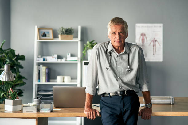 I'm here to help you get better Cropped portrait of a handsome mature male doctor standing in his office general practitioner stock pictures, royalty-free photos & images