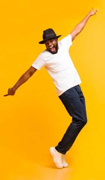 Photo of Funny Black Guy Fooling, Standing on Tiptoes Over Yellow Background