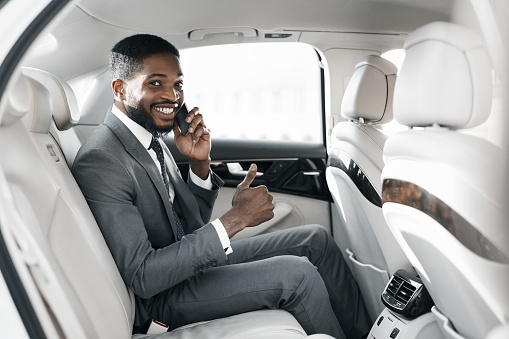 Young afro businessman in luxury car, showing thumb up and talking on cellphone