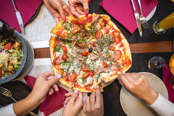 mujeres jóvenes tomando una rebanada de pizza cada una en un restaurante - pizza party fotografías e imágenes de stock