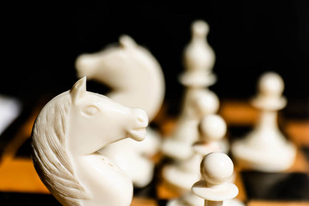 Close-up view of white chess pieces on a wooden chessboard in a scattered game. Isolated on black background.