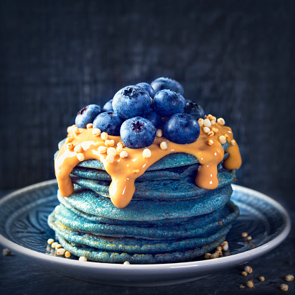 Blue spirulina pancakes topped with peanut butter, blueberries and popped quinoa