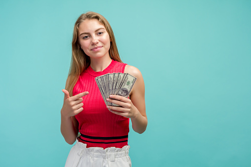 Portrait of a smiling girl pointing at bunch of money USA banknotes
