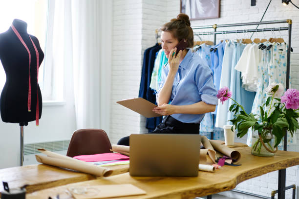 istock Concentrated female dressmaker having working mobile conversation tailoring clothes in showroom, professional couturier booking textile for producing new collection using modern technology in studio 1171081345