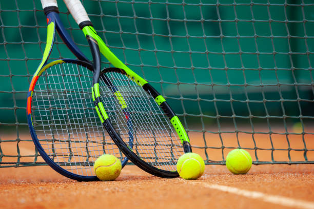 raquetas de tenis y pelotas apoyadas contra la red. - tennis tennis racket racket tennis ball fotografías e imágenes de stock