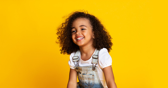 Laughing cute afro girl portrait, kid hearing joke over yellow studio background