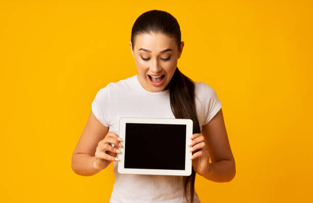 istock Surprised Girl Holding Tablet Looking At Empty Screen, Yellow Background 1171085904