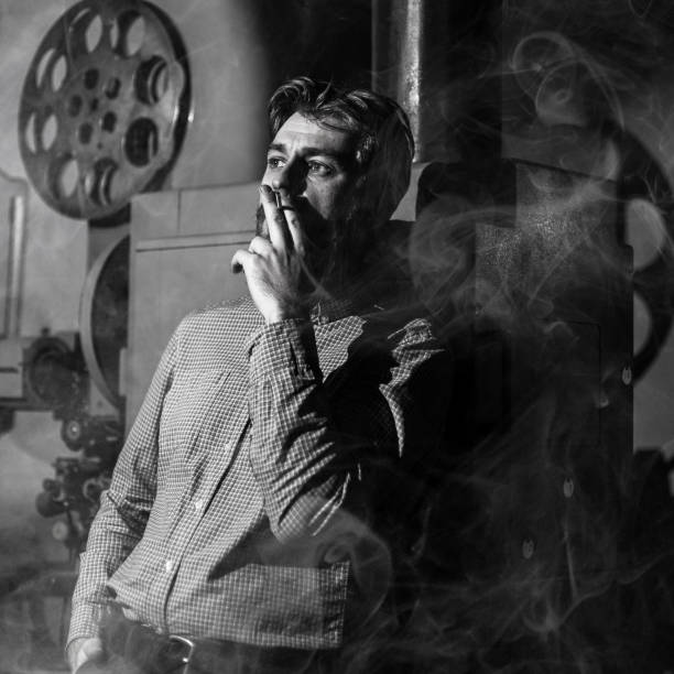 foto in bianco e nero di un proiezionista stanco che fuma in una sala cinematografica. è tutto nel fumo. - projectionist foto e immagini stock