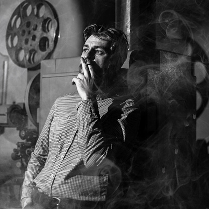 Black and white photo of a tired projectionist smoking in a movie room. Everything is in the smoke. Tobacco Harm Concept