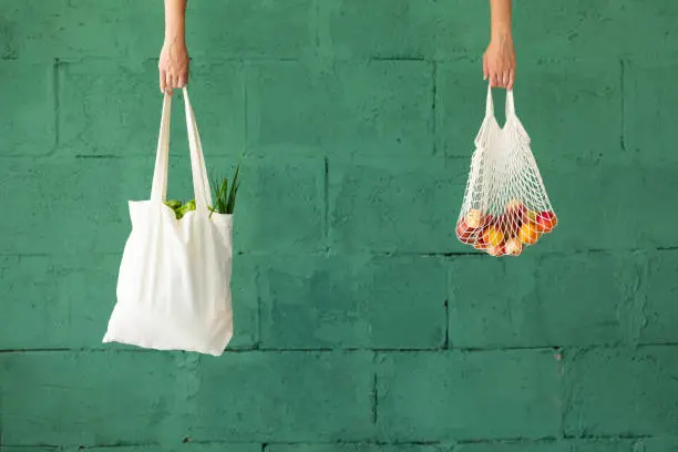 Photo of Female hands with shopping cotton mesh eco bag on green background. Zero waste concept