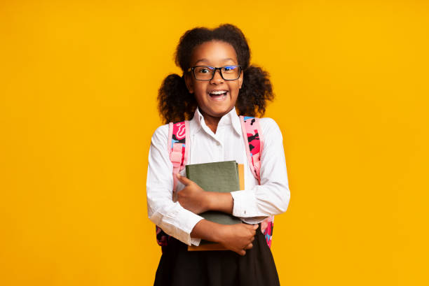 istock Happy elementary student girl embracing books on yellow studio background 1171088210