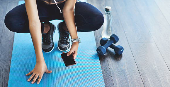 Closeup shot of a sporty woman using a cellphone while exercising in a studio
