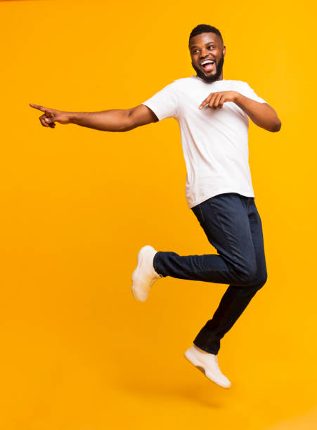 Joyful millennial guy jumping on air and pointing aside Joyful black millennial guy jumping on air and pointing aside, free space moving down photos stock pictures, royalty-free photos & images