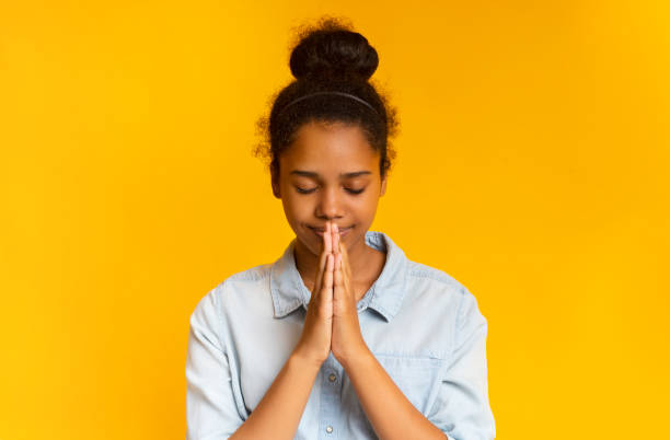 concentrated african girl praying with hands clasped near face - praying girl imagens e fotografias de stock