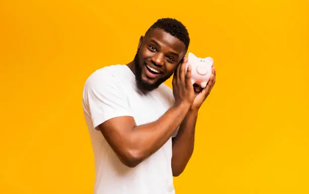 Photo of Happy african american man shaking full piggy bank