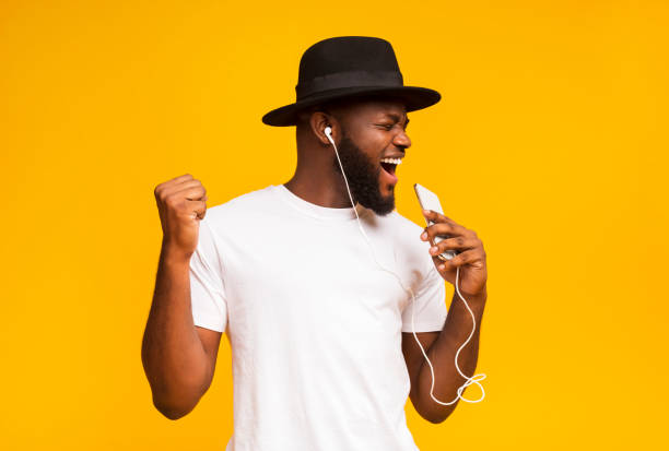 hombre africano feliz en sombrero cantando en el teléfono inteligente como micrófono - musical feel fotografías e imágenes de stock