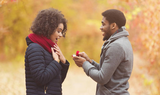 romantico uomo afro che propone alla donna nel parco autunnale - hairstyle love wedding photography foto e immagini stock