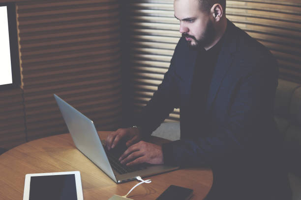 istock Young managing director is writing an advertisement on the Internet through a laptop computer about finding financial expert, while is sitting in office interior near screen with mock up copy space 1171098774