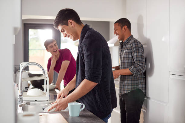 Group Of Male College Students In Shared House Kitchen Washing Up And Hanging Out Together Group Of Male College Students In Shared House Kitchen Washing Up And Hanging Out Together roommate stock pictures, royalty-free photos & images