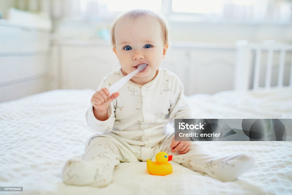 Cute little girl with toothbrush in pyjamas on bed Cute little girl in pyjamas on bed. Happy kid cleanng her teeth with dental brush Baby - Human Age Stock Photo
