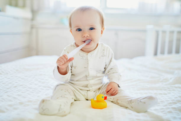 Cute little girl with toothbrush in pyjamas on bed stock photo