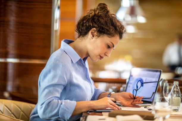 mujer propietaria de pequeñas empresas haciendo un informe financiero de su empresa a partir de un gráfico circular en su computadora portátil mientras estaba sentada en un restaurante exclusivo - bureaucracy fotografías e imágenes de stock