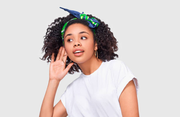 African American young woman paying attention and placing hand on ear asking someone to speak louder or whisper, isolated on white wall. Pretty Afro girl which overhears secret conversation stock photo