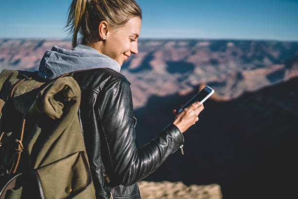 Smiling female tourist with backpack blogging in networks using good mobile connection in arizona national park,hipster girl checking mail on smartphone hiking in wild nature carrying rucksack