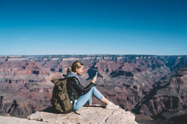 istock Smiling girl with rucksack using mobile connection for sending messages from rocky cliff in National Park, female tourist wanderlust checking mail on cellular resting during hiking on mountain top 1171124255