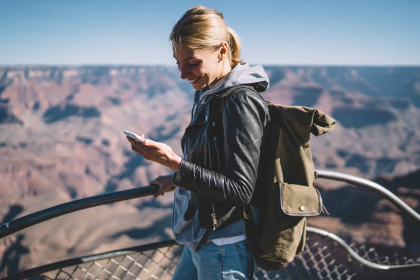 istock Smiling female explorer reading message on telephone satisfied with mobile connection during hiking tour,cheerful  girl wanderlust using cellular chatting standing on viewpoint in Grand Canyon 1171124262