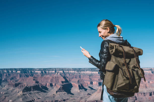 istock Smiling female explorer standing on breathtaking Grand canyon scenery reading message on smartphone happy about good connection, girl wanderlust with backpack checking cellphone mail in roaming 1171124266