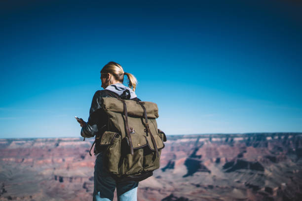 istock Back view of female hiker with backpack holding cellphone checking mobile network connection explore Grand canyon, girl wanderlust reading new message from friend on telephone using roaming 1171124288