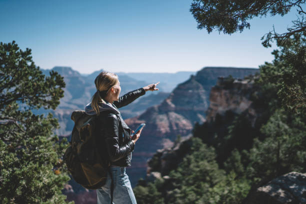 istock Positive female traveler with backpack satisfied with application for checking direction during route exploring wild nature in USA ,hipster girl pointing on high mountain holding smartphone in hand 1171124318