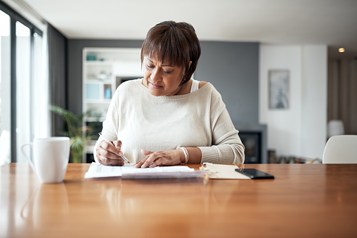Cropped shot of a mature woman working through paperwork while sitting at home
