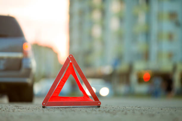 istock Red emergency triangle stop sign and broken car on a city street. 1171124862