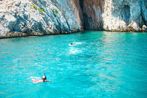 Seascape view to turquoise waters of Aegean Sea in Island Moni near Athens, blue caves. Famous travel sailing destination Greece, Saronic gulf summer scenery Europe. People dive with flippers and mask