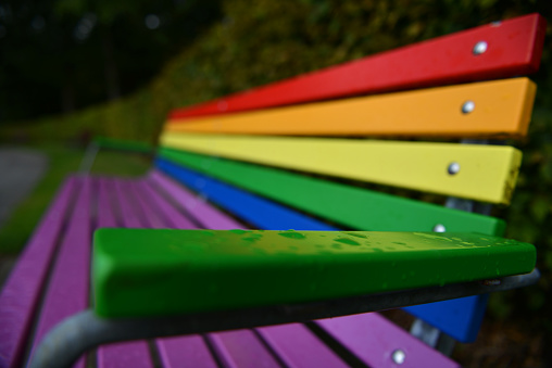 Public bench painted in Rainbow Pride colors with raindrops in the foreground in Denmark.