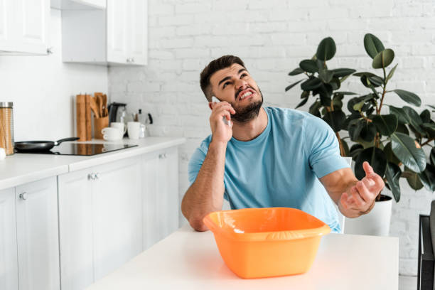 angry bearded man talking on smartphone near plastic wash bowl - roof leak imagens e fotografias de stock