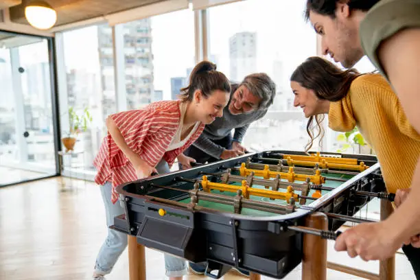 Happy group of people at the office relaxing a while playing foosball all having fun