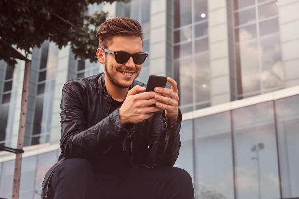 istock Smiling attractive man is chatting on mobile phone while sitting outside near building 1171133322