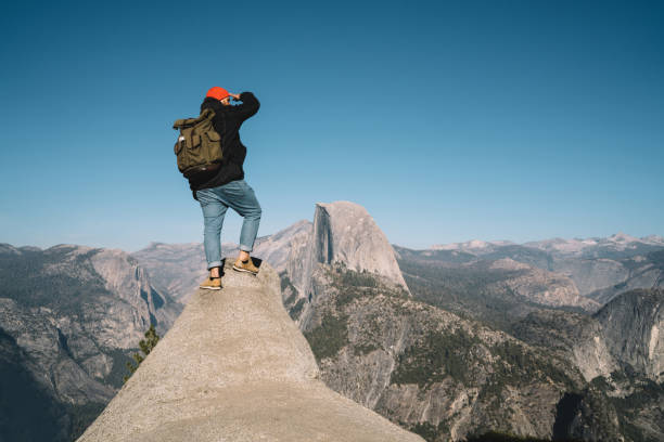 Hipster guy standing on rocky cliff over deep abyss observing landscape for tracking route from top, male traveler with backpack getting to mountain top exploring lands during weekend hiking tour tipo hipster de pie en un acantilado rocoso sobre el abismo profundo observando el paisaje para rastrear la ruta desde la cima, viajero masculino con mochila llegando a la cima de la montaña explorando tierras durante la excursión de senderismo de fin de