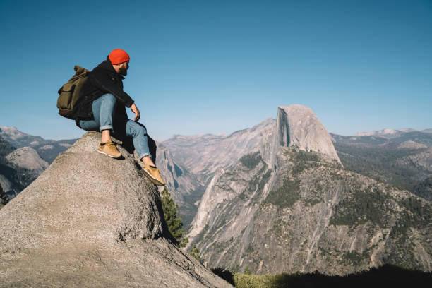 Young hipster guy enjoying wanderlust hiking tour getting to mountain top for observing breathtaking view,male traveler sitting on rocky cliff over abyss enjoying exploring wild environment in usa joven hipster chico disfrutando de paseo excursion de senderismo llegar a la cima de la montaña para observar la vista impresionante, viajero masculino sentado en un acantilado rocoso sobre el abismo disfrutando de explorar el entorno salvaje en nosotros
