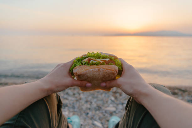 Young woman resting with fast food burger by the sea, pov. stock photo