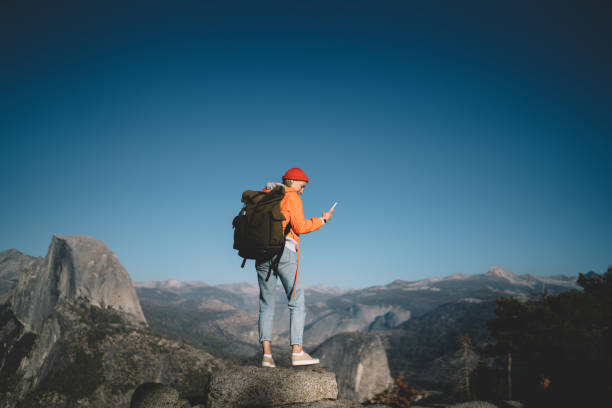 istock Young female traveler with backpack standing on rock cliff holding cellular getting new message using good mobile connection,woman wanderlust getting to mountain top via app on smartphone and network 1171140022