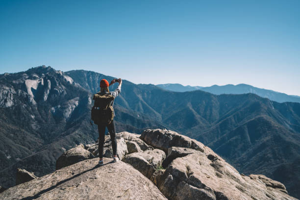 Back view of hipster girl wanderlust using smartphone camera for making selfie on mountain peak, female travel blogger taking picture on telephone on breathtaking landscape scenery of national park vista trasera de la chica hipster wanderlust usando la cámara del teléfono inteligente para hacer selfie en el pico de la montaña, blogger de viajes femenino tomando la foto en el teléfono en el paisaje impresionante paisaje del parque nacional