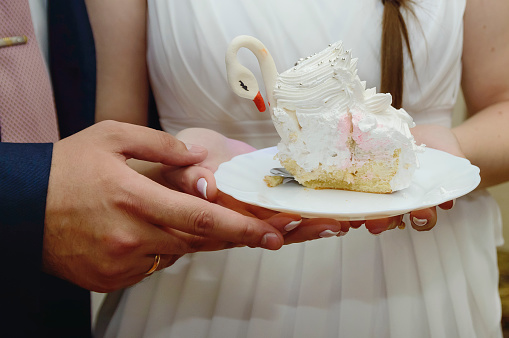 The bride and the groom are holding a piece of wedding cake, close-up.